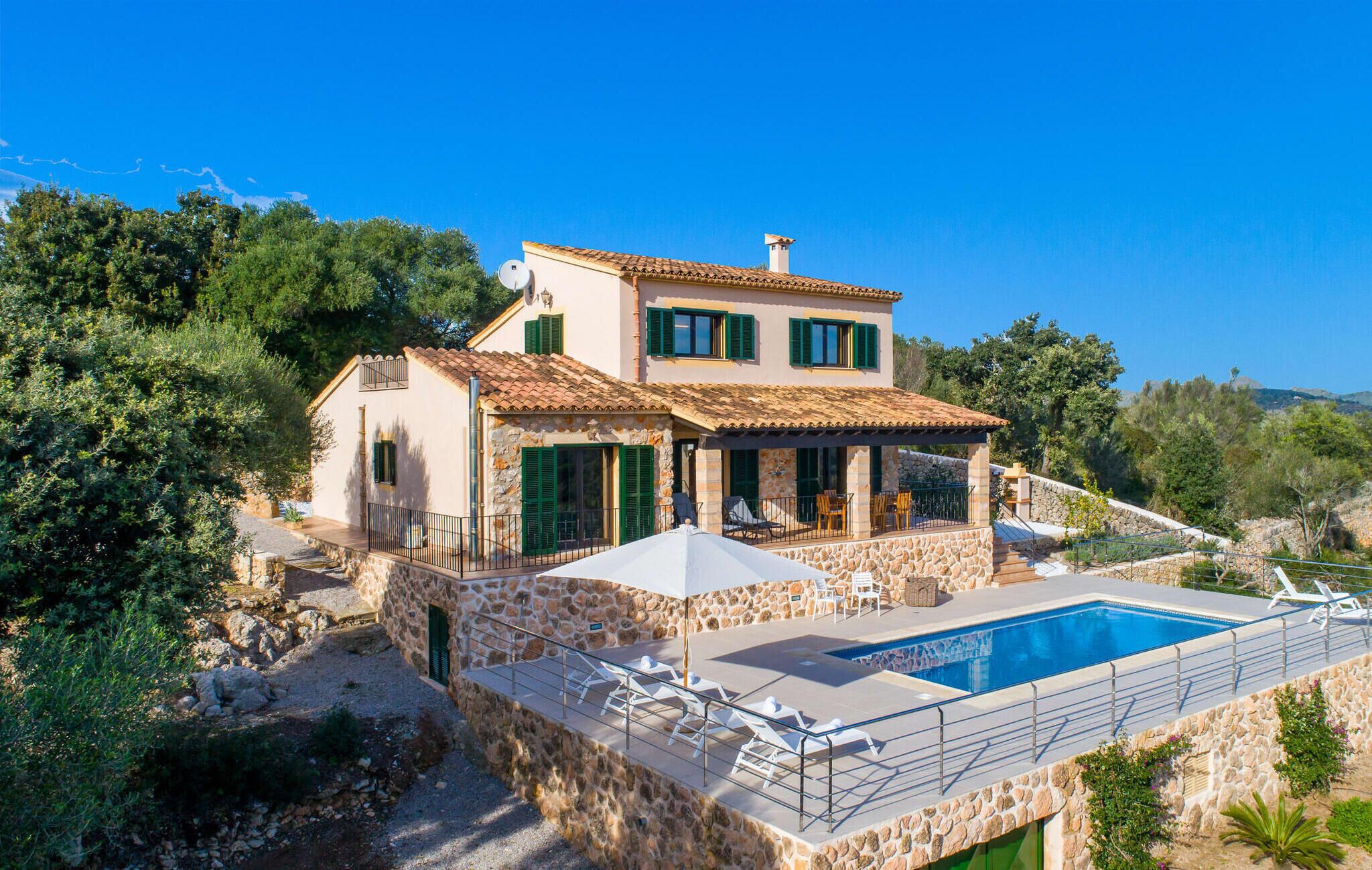 A two-story stone house with a swimming pool, outdoor seating, and a stone staircase.
