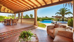 Ein überdachter Außenbereich mit Pool, Korbmöbeln und Blick auf Pool und Grünflächen.