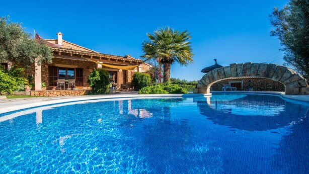 Ein Pool mit einer Steinbogenbrücke, ein Gebäude mit einer Terrasse und eine Palme.