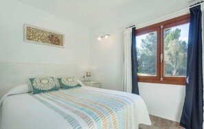 A bedroom with a bed, a nightstand, a window with curtains, and a wall decoration. - Amazing home in Algaida with private swimming pool, can be inside or outside (Algaida)