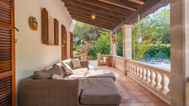 Un espace extérieur aménagé, abrité et doté de mobilier en osier, d’un sol carrelé et offrant une vue sur la verdure.