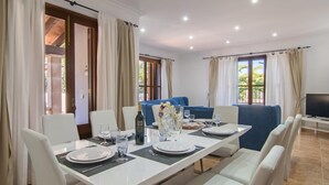 Un coin repas avec une table dressée pour quatre personnes, des chaises blanches, un canapé bleu et un téléviseur posé sur un meuble.