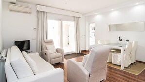 Uma sala de estar moderna com sofá, poltrona e uma área de jantar com mesa e cadeiras.