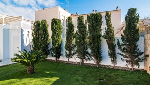 Um edifício moderno com telhado plano, rodeado por um jardim bem cuidado e árvores altas e esguias.