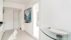 Um corredor com porta de vidro que dá para um banheiro, um quadro com pintura de paisagem urbana e uma pia de vidro com bacia estampada.
