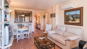 Una sala de estar con un sofá color crema, una mesa de centro de vidrio y un comedor con una mesa y sillas blancas.