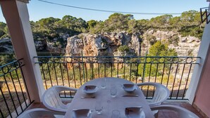 Un balcón con mesa lista para comer, con vista a un acantilado y árboles.