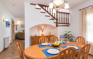 Ein Essbereich mit einem Holztisch, gedeckt für vier Personen, umgeben von Holzstühlen. Eine Pendelleuchte hängt über dem Tisch, und im Hintergrund ist eine Treppe mit Holzspindeln zu sehen.