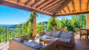 Un espacio de estar al aire libre techado, con mobiliario de mimbre, una mesa de madera y vistas a un paisaje exuberante.