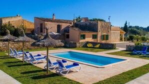 Un espace piscine avec des chaises longues, un mur en pierre et un bâtiment doté d’un toit en tuiles.