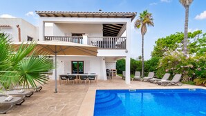 Ein zweistöckiges Haus mit Balkon, Pool und Sitzgelegenheit im Freien.