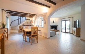 A spacious living area with a dining table, chairs, a staircase, and a kitchen area with a TV. - Lovely home in Cala dOr with private swimming pool, can be inside or outside (Cala dOr)