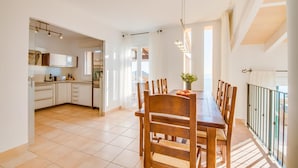 Et rummeligt køkken med moderne hårde hvidevarer, et spiseområde med træstole og en balkon med gelænder.