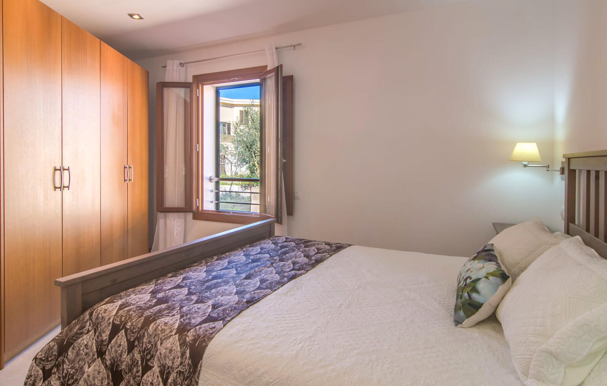 A bedroom with a bed, a wooden wardrobe, a window with curtains, and a balcony view.