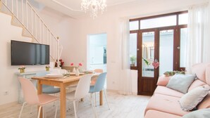 A modern living room with a wooden dining table, white chairs, a pink sofa, and a TV mounted on the wall. - 3 bedroom cozy home in Alcudia (Alcudia)