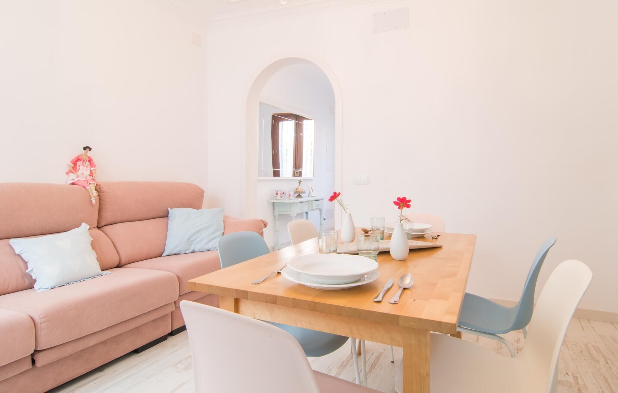Ein Wohnzimmer mit einem rosafarbenen Sofa, einem Holzesstisch mit Stühlen und einer kleinen weißen Kommode.