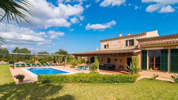 Una vila amb piscina, mobiliari d'exterior i un jardí ben cuidat.