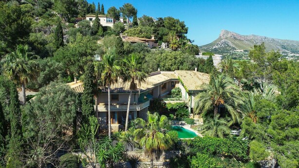 Una villa su una collina con piscina, immersa nel verde e con una montagna sullo sfondo.