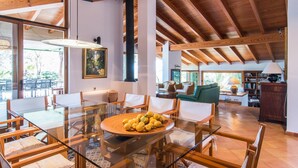 Un'ampia zona giorno con tavolo da pranzo in vetro, arredi in legno e soffitto alto con travi a vista.