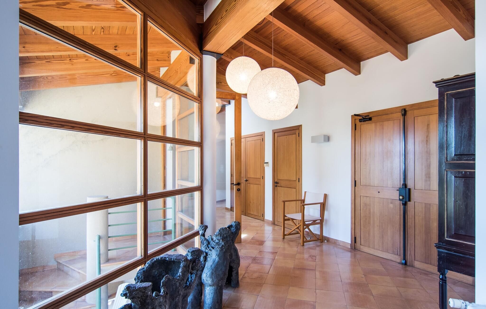 A spacious room with large windows, wooden beams, and a modern chandelier.