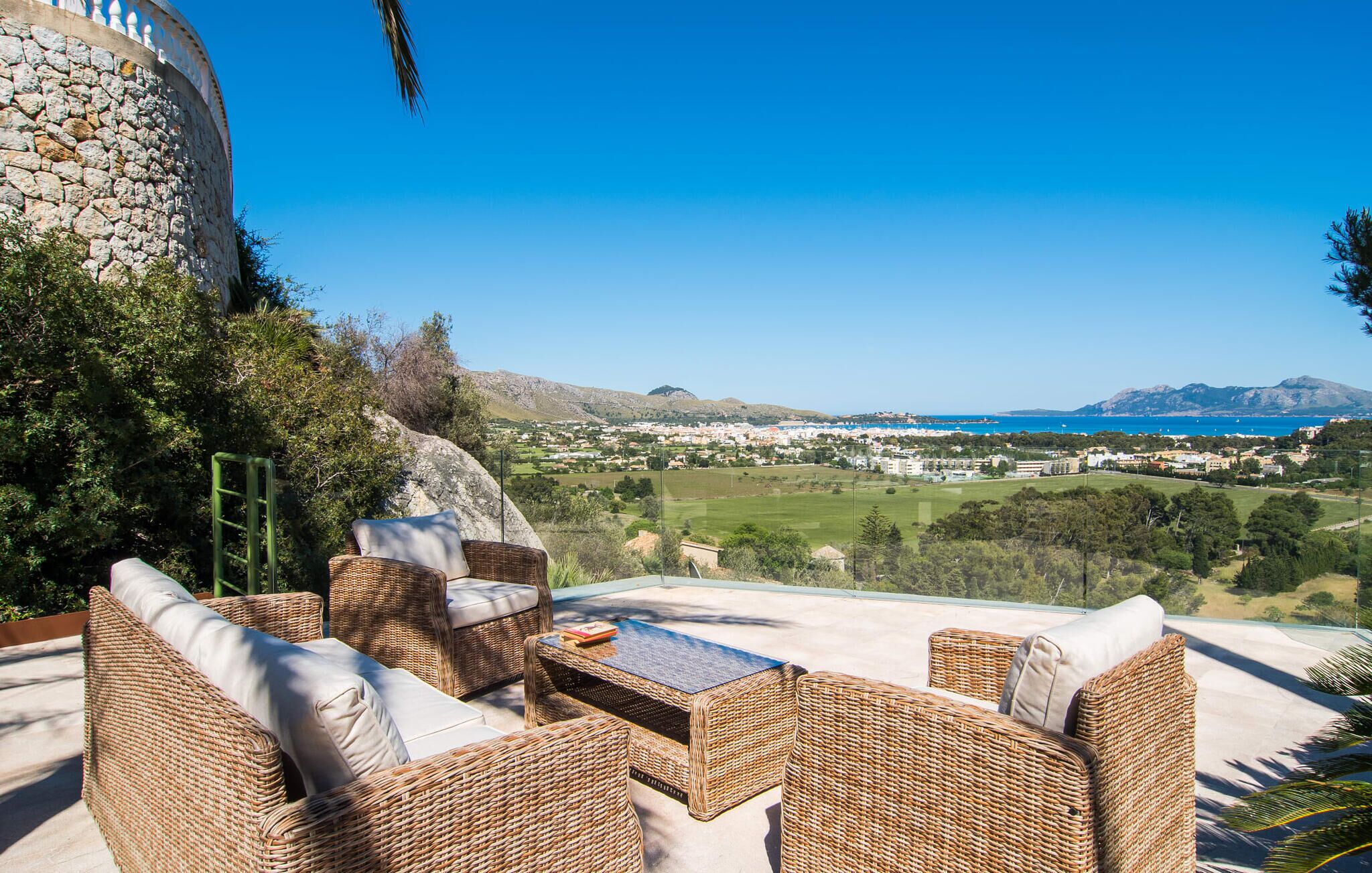 A wicker outdoor seating area with a view of a coastal town and mountains.