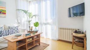 Ein helles Wohnzimmer mit einer Couch, einem Holztisch und einem an der Wand befestigten Fernseher.