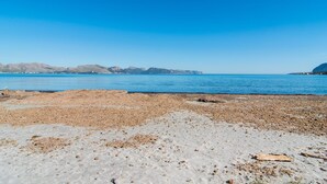 Una playa pedregosa con aguas azules cristalinas y montañas a lo lejos.