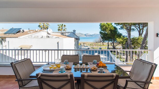 Un balcón con una mesa lista para el desayuno, con vistas a un paisaje que incluye una masa de agua y edificios.