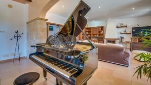 A grand piano in a well-lit living room with a fireplace, bookshelves, and a television. - Lovely home in SHorta with private swimming pool, can be inside or outside (SHorta)