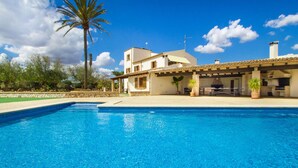 Une piscine avec un espace patio, un bâtiment blanc doté d’un toit en tuiles et un palmier.
