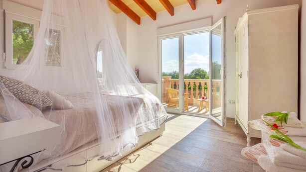 Un dormitorio con una cama con dosel, un balcón con sillas de mimbre y vistas a la vegetación.