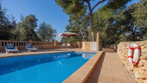 Piscina con sillones de descanso y un flotador adherido a un muro de piedra.