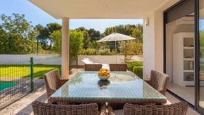 An outdoor patio with a glass-top table, wicker chairs, a bowl of lemons, and a large umbrella. - Awesome home in Cala Ratjada (Cala Ratjada)