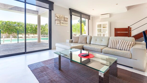 A modern living room with a glass coffee table, a beige sofa, and a view of a pool and greenery outside. - Awesome home in Cala Ratjada (Cala Ratjada)