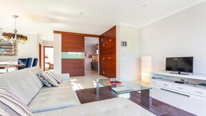 A modern living room with a sofa, glass coffee table, TV, and a dining area with chairs and a table. - Awesome home in Cala Ratjada (Cala Ratjada)