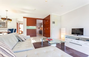 A modern living room with a sofa, glass coffee table, TV, and a dining area with chairs and a table. - Awesome home in Cala Ratjada (Cala Ratjada)