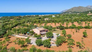 Paisagem rural com um pequeno edifício rodeado de árvores e vista clara para o mar.