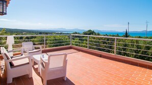 Um terraço com móveis de vime branco, vista para o mar e céu claro.