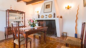 Uma sala de jantar com mesa de madeira, cadeiras, um armário com copos, lareira e arandelas na parede.