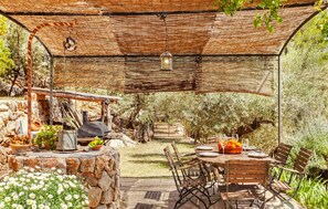 Une terrasse extérieure avec une table en pierre, des chaises en bois et une lanterne suspendue.