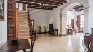 Habitació àmplia amb escala de fusta, zona de dinar amb cadires i taula, i un gran arc d'entrada.