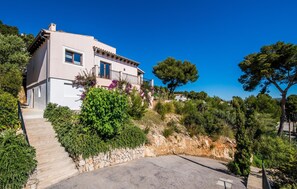 A modern two-story house with a stone staircase leading to the entrance, surrounded by lush greenery and trees. - Stunning home in Canyamel with private swimming pool, can be inside or outside (Canyamel)