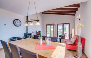 A dining area with a wooden table, chairs, and a chandelier. There is a sofa and a vase with flowers in the background. - Stunning home in Canyamel with private swimming pool, can be inside or outside (Canyamel)