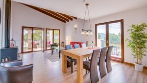 A spacious dining area with a wooden table and chairs, a red sofa, and a large window offering a view of the outdoors. - Stunning home in Canyamel with private swimming pool, can be inside or outside (Canyamel)