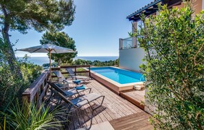A wooden deck with a swimming pool, lounge chairs, and an umbrella. - Stunning home in Canyamel with private swimming pool, can be inside or outside (Canyamel)