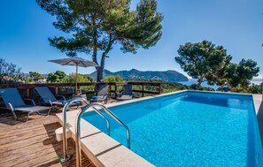 Una piscina amb aigua cristal·lina i blava, envoltada de gandules i ombrelles de fusta, amb vistes a un paisatge idíl·lic de muntanyes i mar.