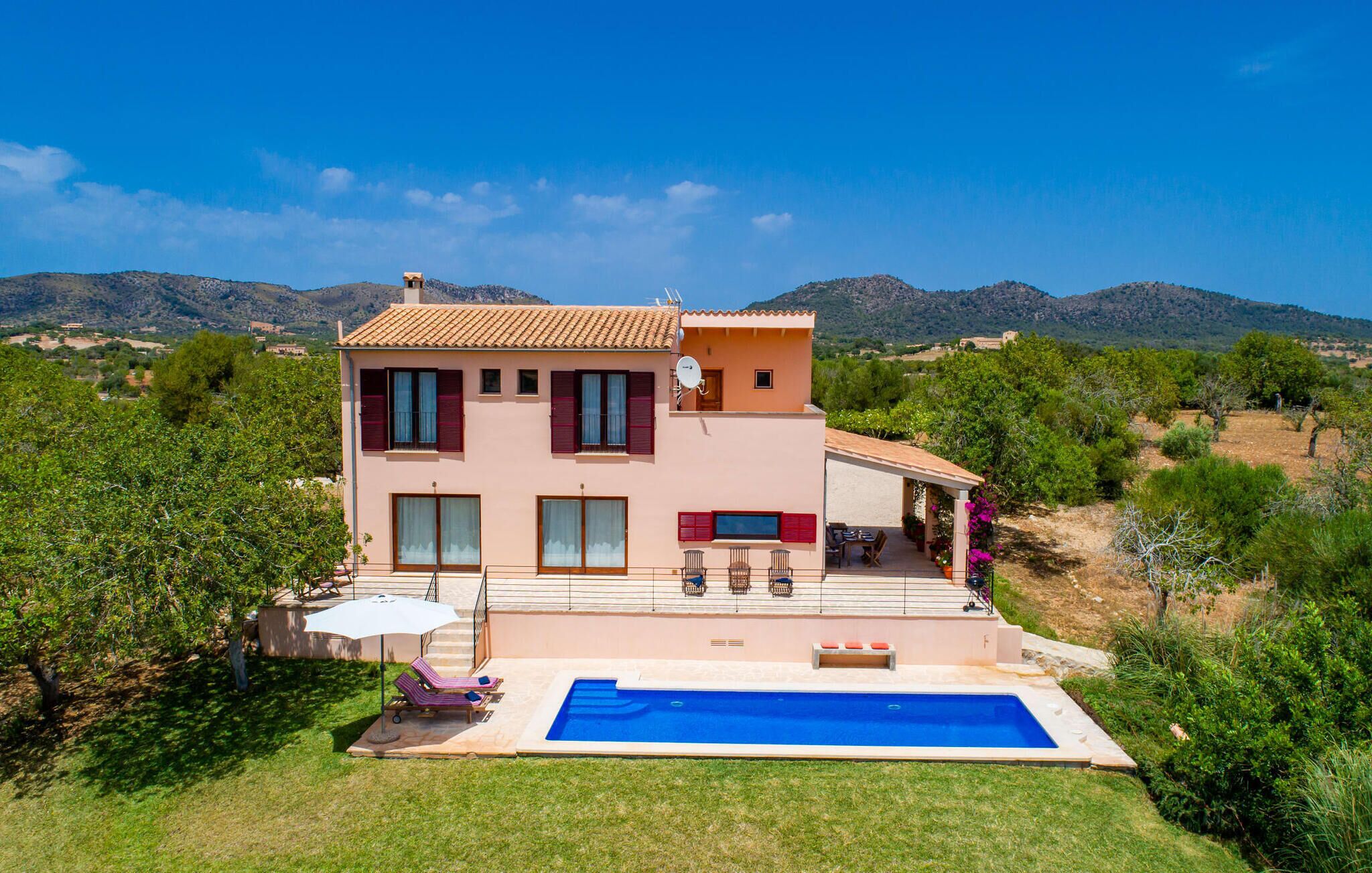 A two-story house with a swimming pool, surrounded by greenery and mountains.