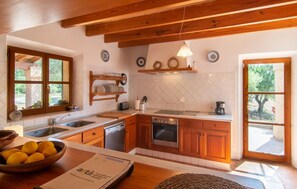 A kitchen with wooden cabinets, a stainless steel sink, and a built-in oven. There are decorative plates on the wall and a bowl of lemons on the counter. - Villa Maria de Betlem (Betlem)