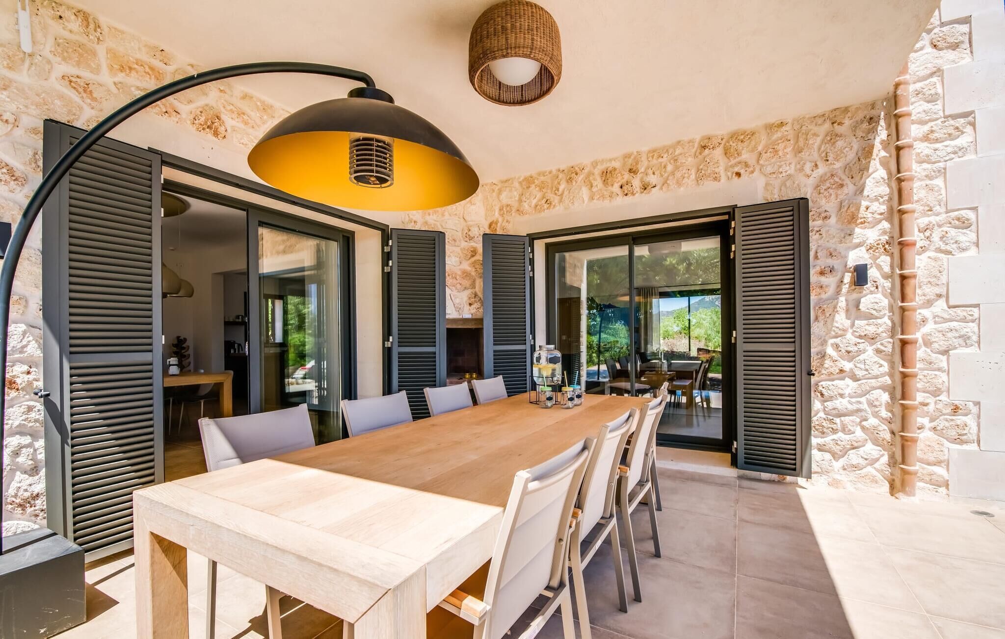 A spacious dining area with a long wooden table, black shutters, and a yellow pendant light.