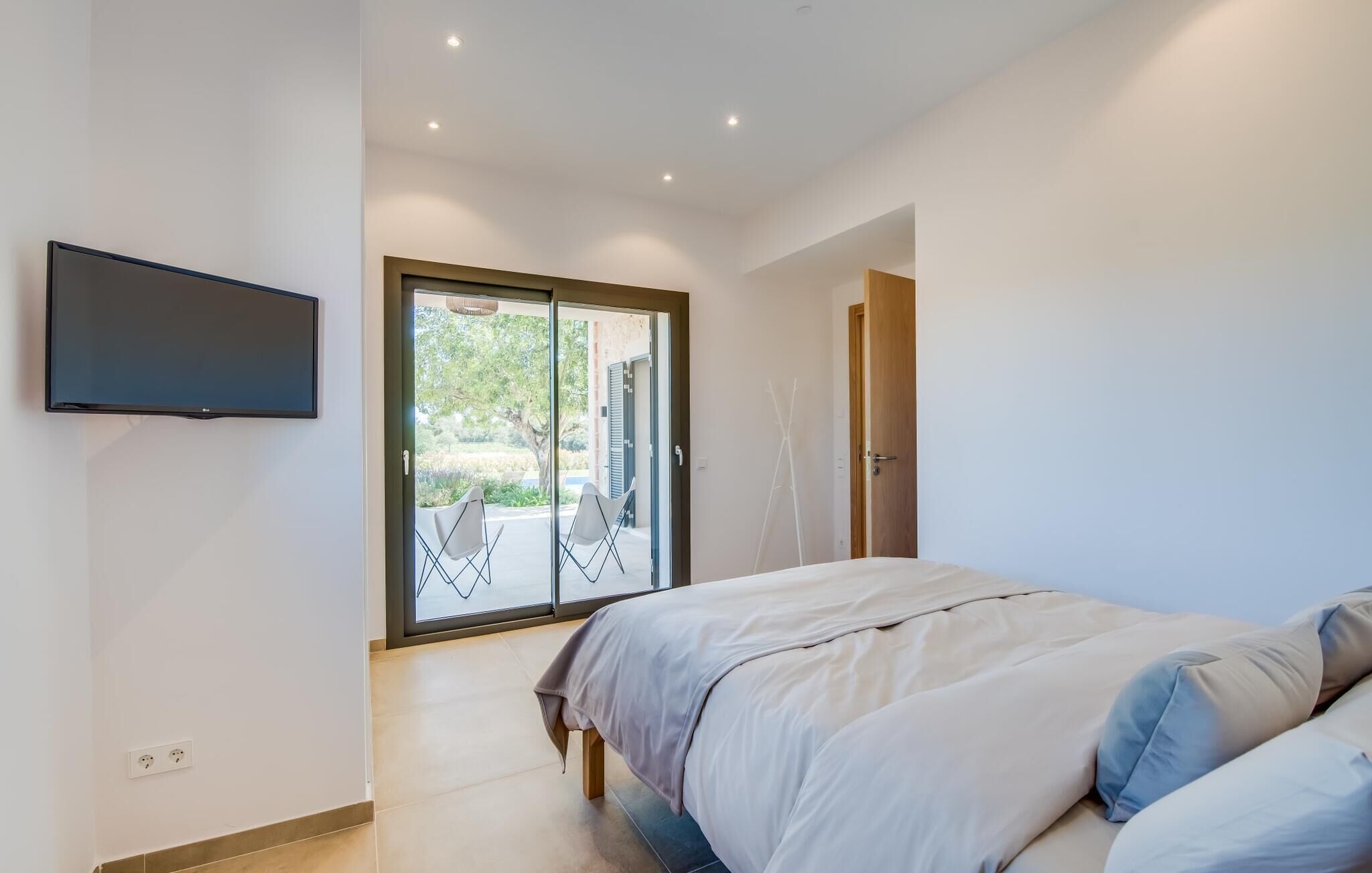 Ein Schlafzimmer mit Bett, einem an der Wand montierten Fernseher und einer Schiebetür zu einem Außenbereich.